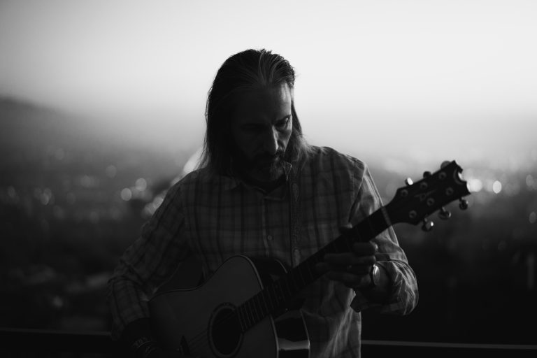 Garrett Gunderson sitting casually and playing an acoustic guitar, black and white style.